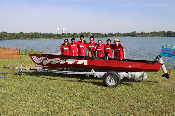 Team members pose behind boat