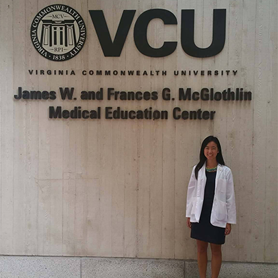 Huang in white coat in front of VCU sign
