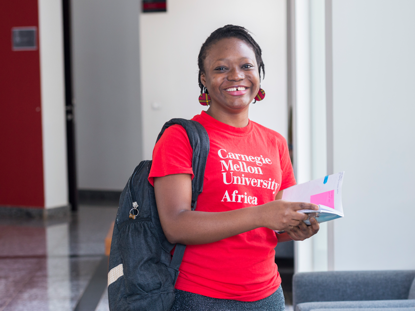 A CMU-Africa student in the halls holding a book